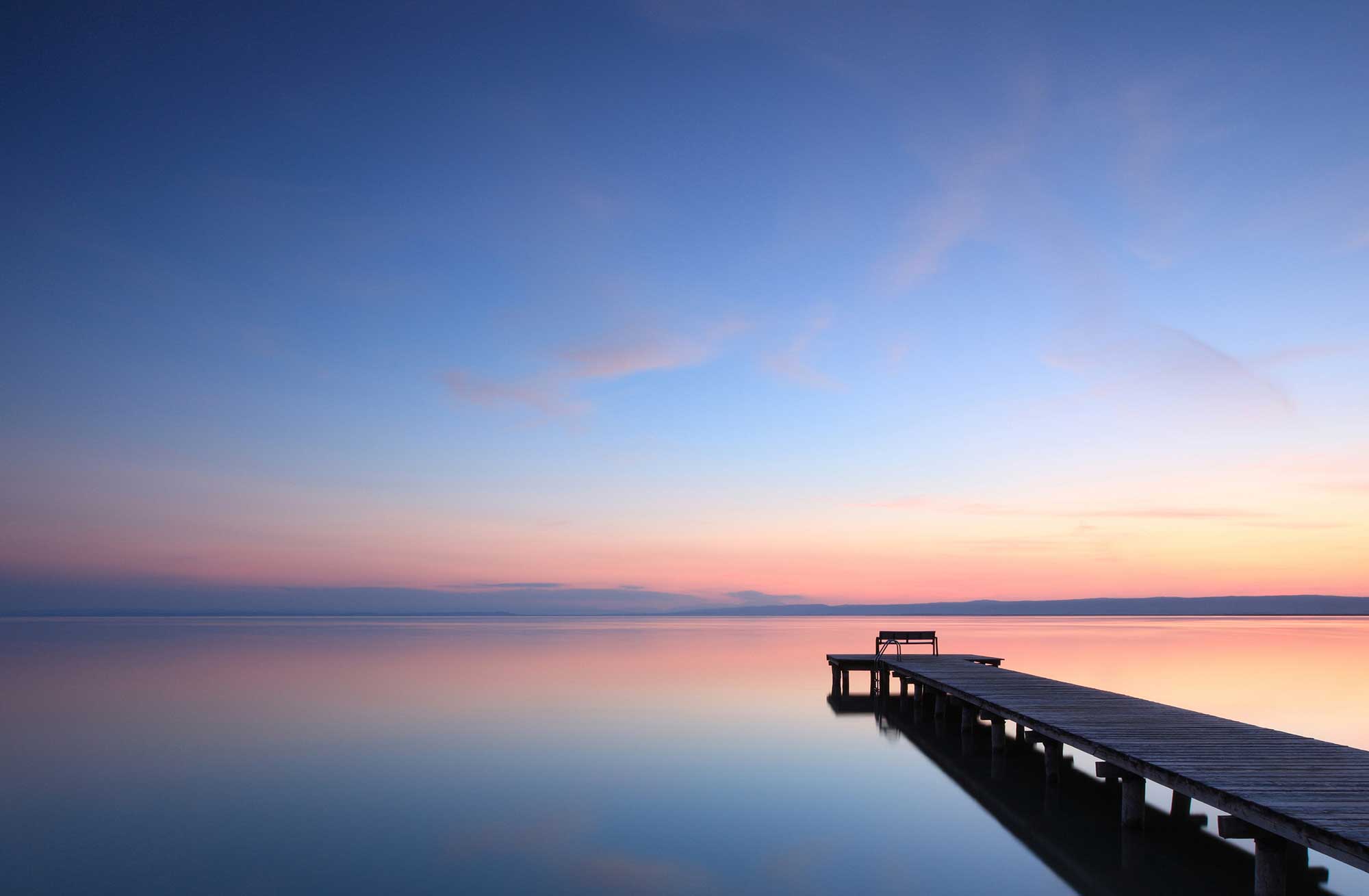 Steg führt weit hinaus auf glatten See in Abendstimmung